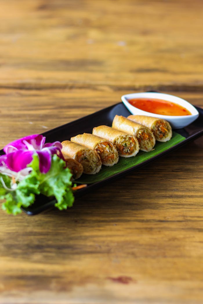 Crispy Thai spring rolls served with a sweet chili sauce, garnished with fresh greens.