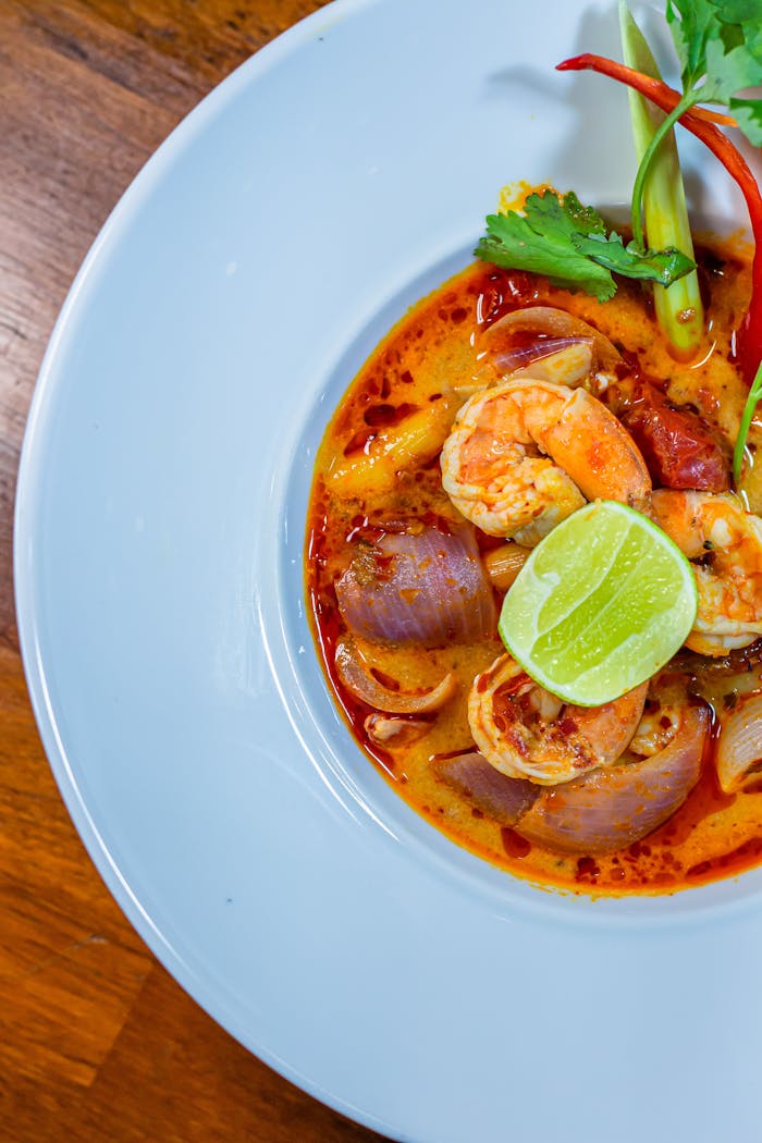 Delicious Thai Tom Yum soup served with fresh prawns, lime, and herbs on a white plate.