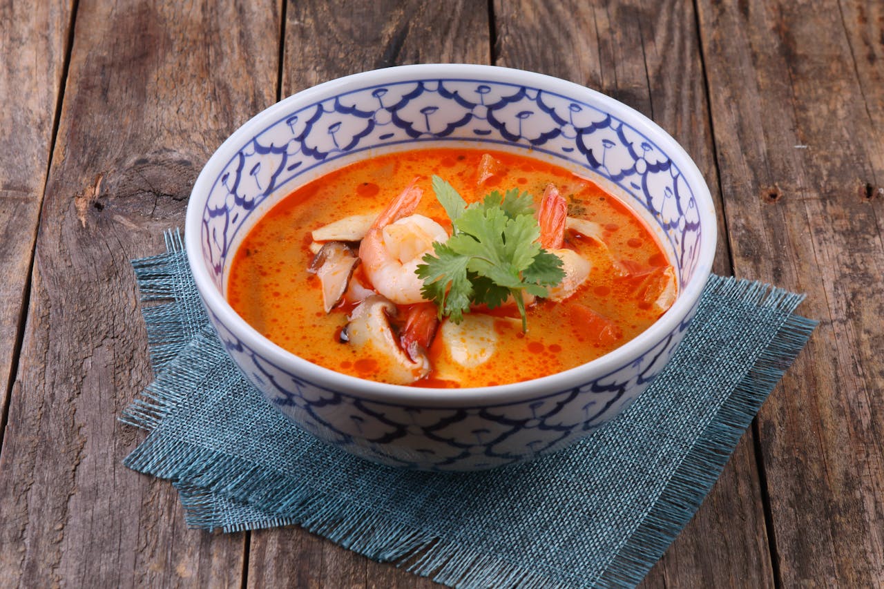 A vibrant bowl of Thai tom yum soup with shrimp and herbs served on rustic wood.